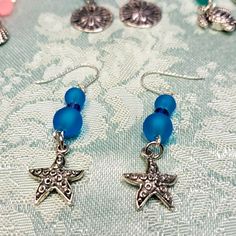 These Pierced Earrings Have Beautiful Blue Sea Glass Beads Separated With Swarovski Blue Bicones. The Starfish Dangle Is Medal And Etched Design On One Side. A Wonderful Gift! Ocean-inspired Blue Jewelry With Star Charm, Blue Jewelry With Star Charm For Jewelry Making, Blue Star Charm Dangle Earrings, Blue Dangle Earrings With Star Charm, Silver Ocean-inspired Earrings With Starfish Charm, Ocean-inspired Silver Earrings With Starfish Charm, Blue Star Charm Drop Earrings, Blue Drop Earrings With Star Charm, Blue Star Charm Earrings For Gift