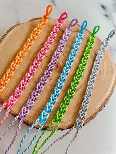 six different colored braided bracelets sitting on top of a piece of wood next to each other