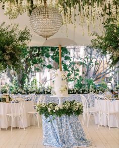 a wedding cake sitting on top of a table under a chandelier filled with greenery