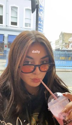 a woman with glasses is holding a drink and looking at the camera while she has her tongue out