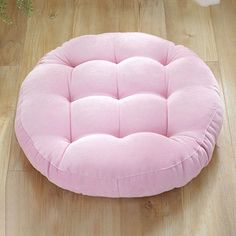 a pink round dog bed sitting on top of a wooden floor next to a potted plant