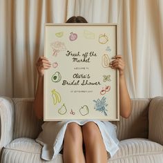 a woman sitting on a couch holding up a framed sign with the words fresh off the market