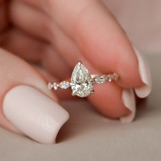 a woman's hand holding a ring with a pear shaped diamond on top of it