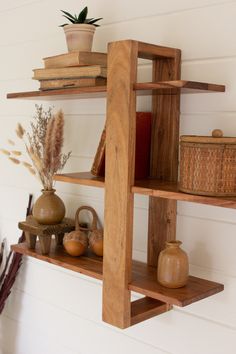 two wooden shelves with books and vases on them against a white wall next to a potted plant