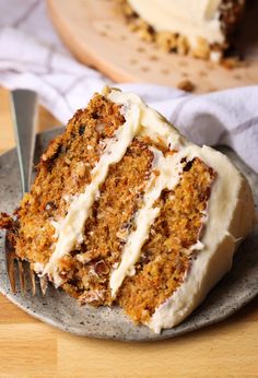 a slice of carrot cake with cream cheese frosting on a plate next to a fork