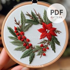 a hand embroidered christmas wreath ornament with holly and poinsettis on it