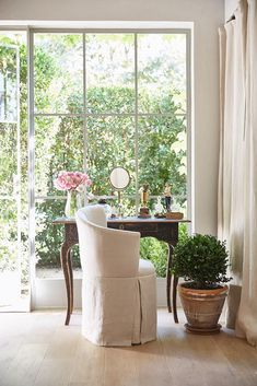 a white chair sitting in front of a window next to a potted plant on top of a wooden table