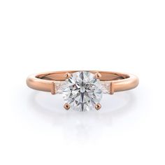 a rose gold engagement ring with two side stones on the band and a round brilliant cut diamond