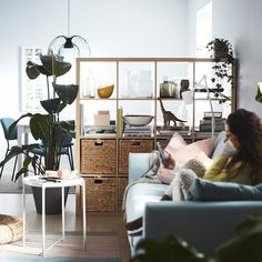 a woman sitting on a couch reading a book in a room with lots of plants