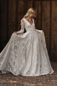 a woman in a white wedding dress is standing on a brick floor and wearing a long sleeved gown