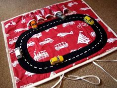 a play mat with cars and trucks on it, sitting on the floor next to a cord