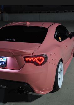 a pink car parked in a parking lot with its tail lights turned on at night