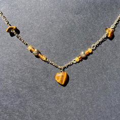 This handmade necklace features a delicate gold chain adorned with a striking heart-shaped, tiger's eye gemstone pendant with bead and gemstone accents along the chain. The warm, earthy tones of the tiger's eye stones add a natural elegance to this unique piece. Perfect for those who love boho and nature-inspired jewelry, this necklace complements any outfit with its rich colors and sophisticated design. The high-quality materials and craftsmanship make it a wonderful gift for birthdays, anniversaries, or any special occasion. Wear it alone for a subtle statement or layer it with other necklaces for a more bohemian look. This is a new shop so please don't be discouraged by the low amount of orders and reviews at this time. Feel free to reach out with any questions, comments, or concerns! Gold Necklaces With Heart Charm And Round Beads, Gold Heart-shaped Beaded Necklaces, Gold Beaded Heart Necklace Gift, Gold Beaded Heart Necklace For Gift, Gold Heart-shaped Beaded Necklace, Dainty Heart-shaped Beaded Necklaces, Dainty Heart-shaped Beaded Necklace, Spiritual Heart Beads Pendant Necklace, Gold Heart-shaped Necklace With Beaded Chain