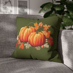 a green pillow with three pumpkins and autumn leaves on it sitting on a couch