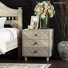 a white bed sitting next to a vase with flowers in it on top of a wooden floor