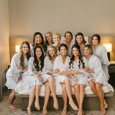 a group of women sitting on top of a bed in white bathrobe outfits