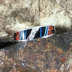 This beautiful Sterling Silver Ring, as part of the Red Moon Collection, features Black Jade, Kingman Turquoise and Blue, Green & Red Lab Opal. with a cascade of three small Cubic Zirconia in the center. Ring Width: 5/16" The ring is designed by David Rosales, one of the finest contemporary Southwest Artists in the world. He is the founder and co-owner of Supersmiths, Inc. of Gallup, NM. Each ring is custom made and carries a lifetime guarantee. Red Sterling Silver Jewelry With Inlay, Red Inlay Ring, Red Ring With Inlay, Multicolor Inlay Rings For Anniversary, Red Inlay Ring Jewelry, Anniversary Multicolor Inlay Rings, Unique Red Diamond Jewelry, Red Sterling Silver Rings With Inlay, Red Sterling Silver Ring With Inlay