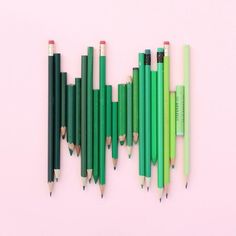 several green pencils are lined up on a pink surface with the same one in between them