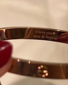 a close up of a person's hand holding a bracelet with the words i love you now and forever on it