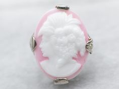 Sweet and full of detail, this Art Deco cameo ring is something special! The filigree is impressive, created using the die-stamping method that produces very fine detail while remaining strong and resilient. The pink glass cameo depicts a woman with 1920s styling, flowers set in curls, and an open neckline. Metal: 14K White Gold Gem: Glass Cameo Gem Measurements: 13.1 x 18.0 mm, Oval Ring Size: 3.25 SKU #: A36203 Each piece has been identified and graded by a Graduate Gemologist who has been cer Elegant Carved White Gold Rings, White Carved Jewelry For Wedding, White Oval Rings With Intaglio, Luxury Cameo Ring Jewelry, White Intaglio Ring Jewelry, Fine Carved Jewelry For Weddings, White Intaglio Ring, White Intaglio Ring As Gift, Carved Fine Jewelry For Wedding