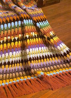 a multicolored crocheted blanket on a wooden floor next to a chair