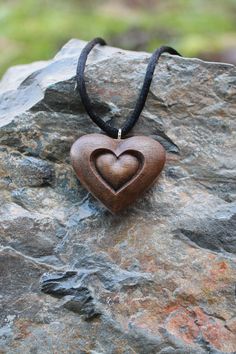 a heart shaped wooden pendant on a black cord necklace sitting on top of a rock