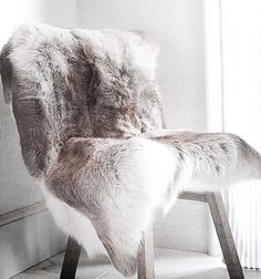 a chair with fur on it sitting in front of a wall next to a window