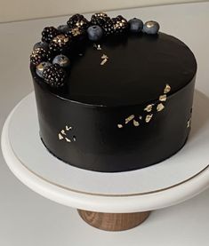 a black cake topped with berries and gold sprinkles on top of a white plate