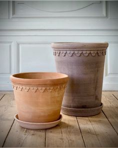 two clay pots sitting side by side on a wooden floor in front of a white wall