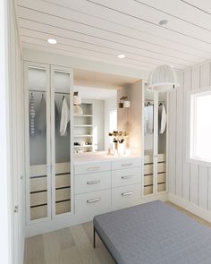 a bed sitting in a bedroom next to a white closet filled with drawers and cabinets