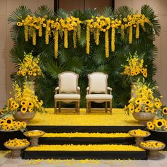 two white chairs sitting in front of a yellow flower covered stage with sunflowers