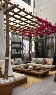 an outdoor living area with couches, tables and flowers on the pergolated roof