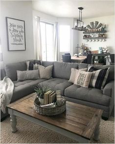 a living room with gray couches and pillows on the coffee table in front of a window