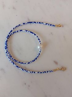 a blue and white beaded lanyard with a gold cross charm on a marble surface