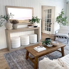 a living room filled with furniture and plants on top of a wooden table in front of a window