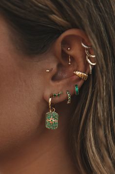 a close up of a person wearing ear cuffs and piercings with green stones on them