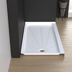 a white shower pan sitting on top of a wooden floor next to a black wall