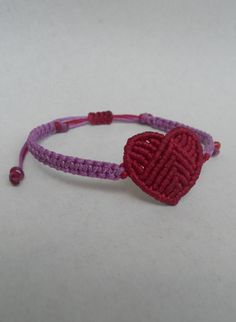 a red and purple bracelet with a small heart on it's end, sitting on a white surface