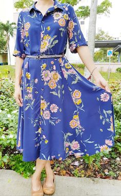 a woman wearing a blue dress with flowers on it standing in front of some bushes