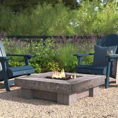 a fire pit sitting in the middle of a gravel field next to two blue chairs