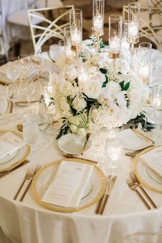 the table is set with white flowers and gold rimmed place settings for dinner guests