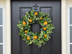 a wreath with oranges and greenery hangs on the front door of a house