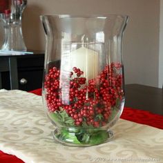 a glass vase filled with red berries and a lit candle sitting on top of a table