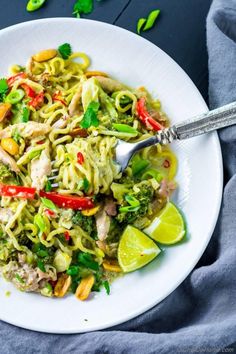 a white plate topped with noodles and vegetables next to lime wedges on a blue table cloth