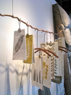 several tea towels hanging from a branch in front of a white wall with leaves on them