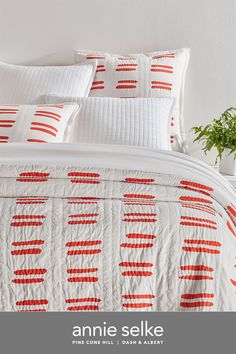 an orange and white quilted bed in a bedroom with plants on the nightstand next to it