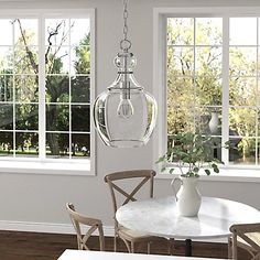 a dining room table with chairs and a vase on the table in front of two windows