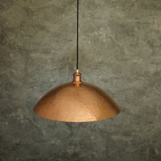 a large copper colored light hanging from a metal ceiling fixture on a concrete wall background