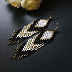 a pair of black and white beaded earrings on top of a table next to flowers