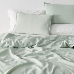 an unmade bed with green sheets and pillows